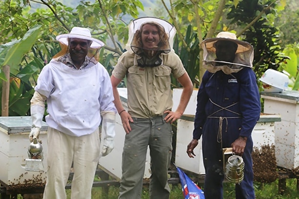 Three men standing together outdoors wearing safety nets in beekeeping outfits