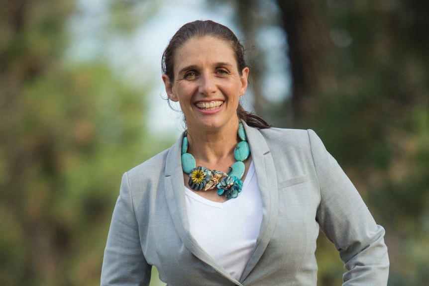 A woman in a business jacket smiles at the camera.