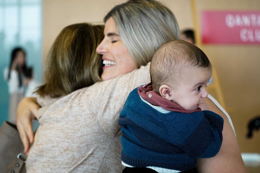 Two women hug, one with a delighted baby in her arm.