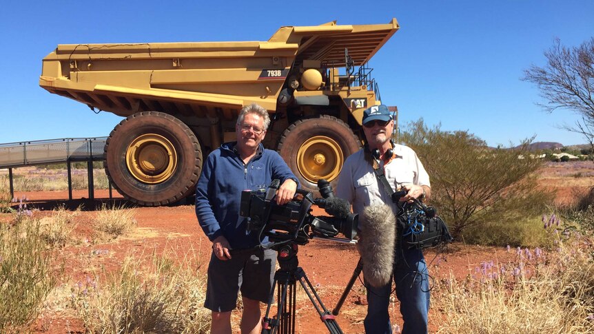 Cameraman Ron Ekkel and sound recordist John Peterson standing in front of giant mining truck in the Pilbara.