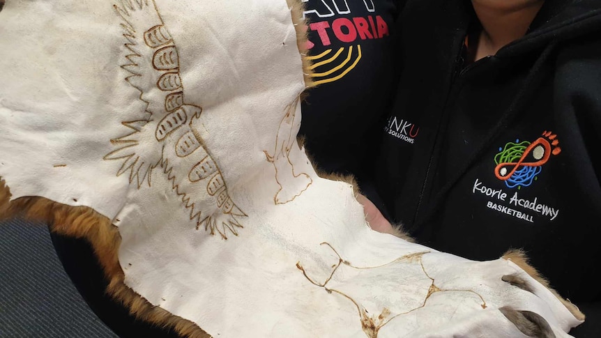 A woman holds up a possum skin with animal motifs stenciled in