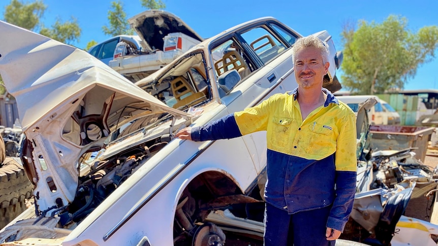 A man in high vis work clothes stands next to a white car wreck