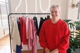 Carla Woidt smiling as she stands in front of a rack of clothing.