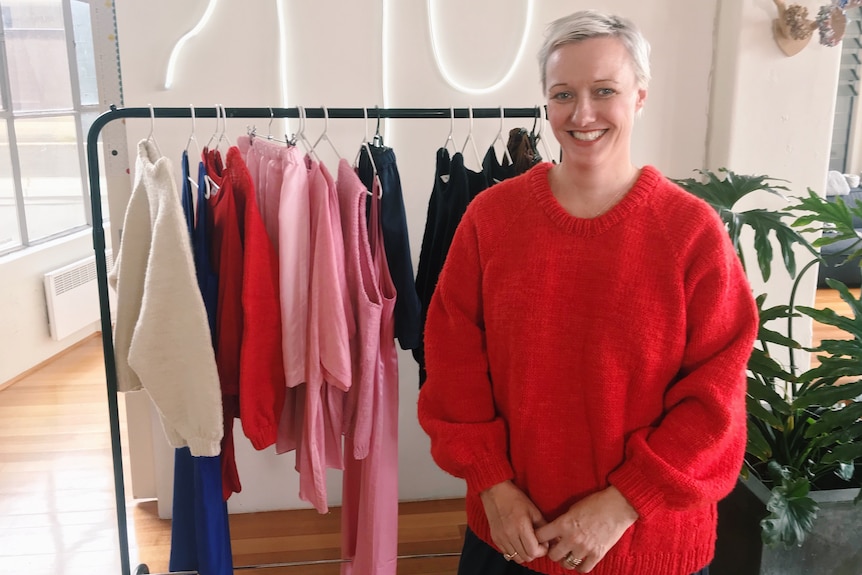 Carla Woidt smiling as she stands in front of a rack of clothing.