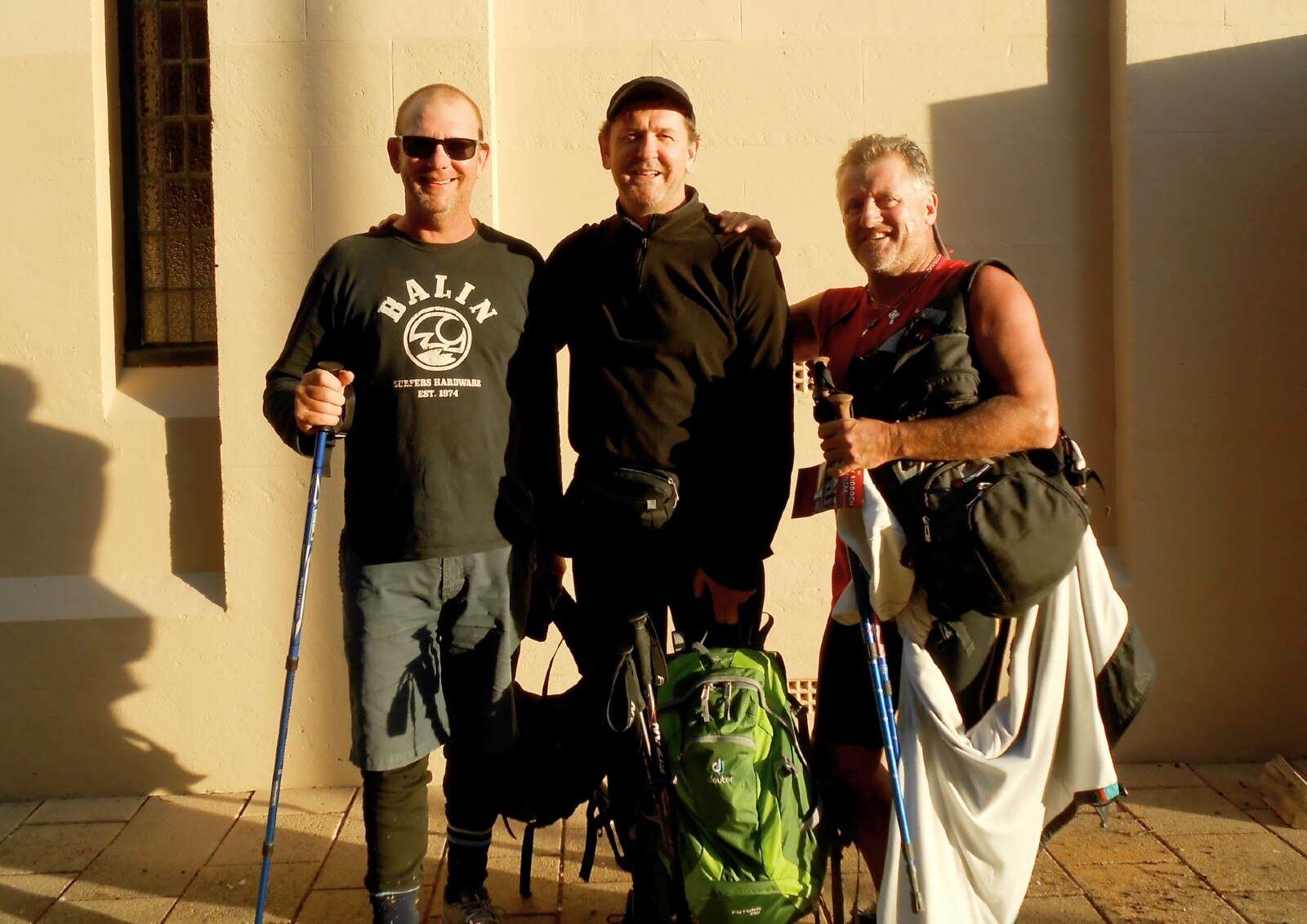 Three men in walking gear stand by a building with a sign reading 'Mary Mackillop Heritage Centre'.