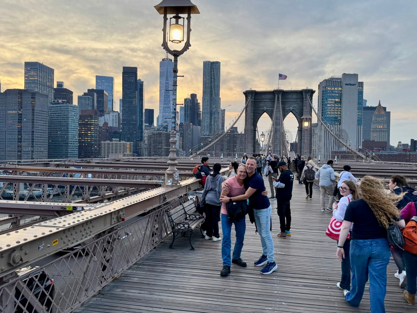 Two men embrace while standing on a bridge with the city skyline behind them