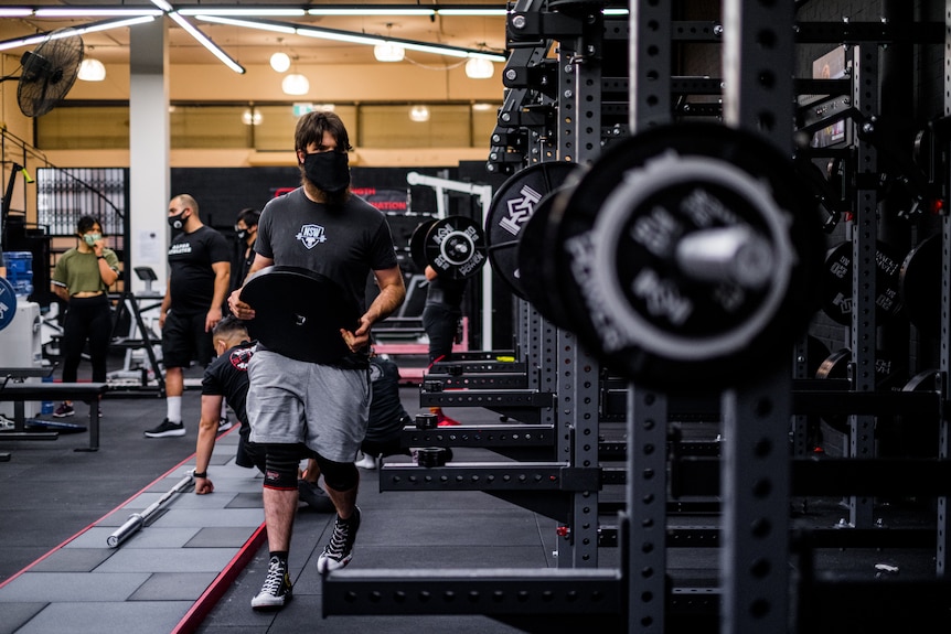 a man carrying a weight wearing a mask inside a gym