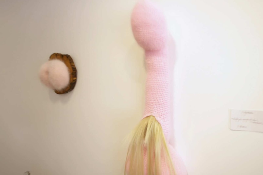 A woolen art piece hangs on a wall in a gallery.