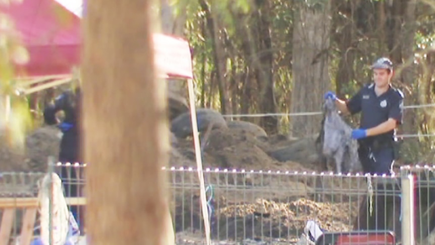 A policeman beside a mound of earth on a bush property holding a piece of material