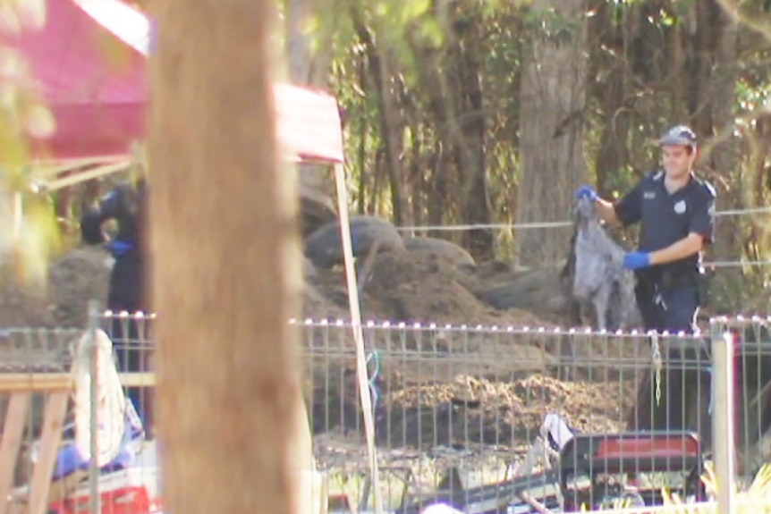 A policeman beside a mound of earth on a bush property holding a piece of material