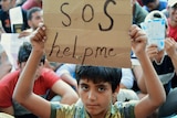 A migrant boy holds a sign reading 'SOS help me' in Budapest