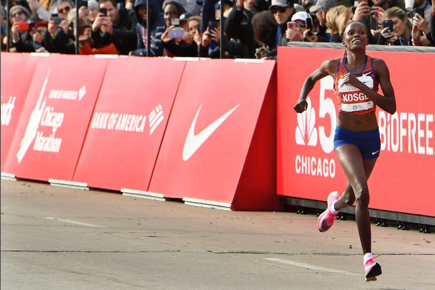 A smiling athlete approaches the end of a marathon run, as the crowd takes pictures of her.