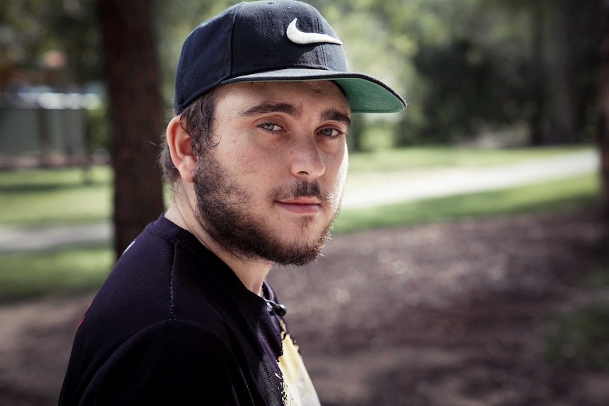 A young man sits on a bench with a hat on.