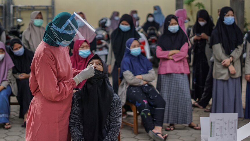 A medical worker collects a swab sample as other young women wait to be tested