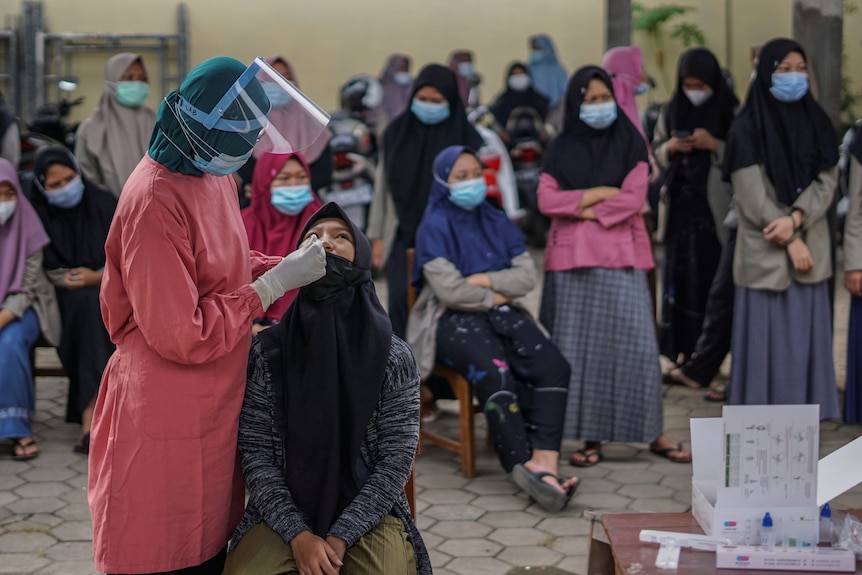 Seorang paramedis mengumpulkan sampel usap sementara wanita muda lainnya menunggu pemeriksaan