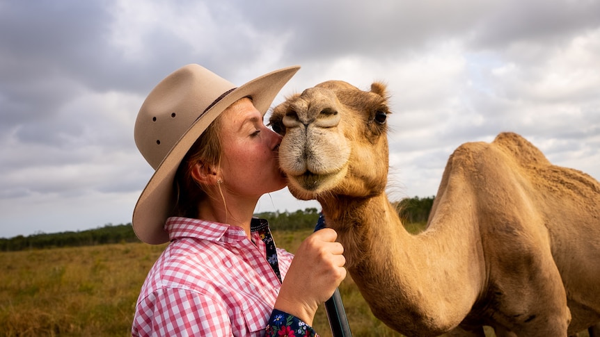 Photo of a woman kissing a camel.