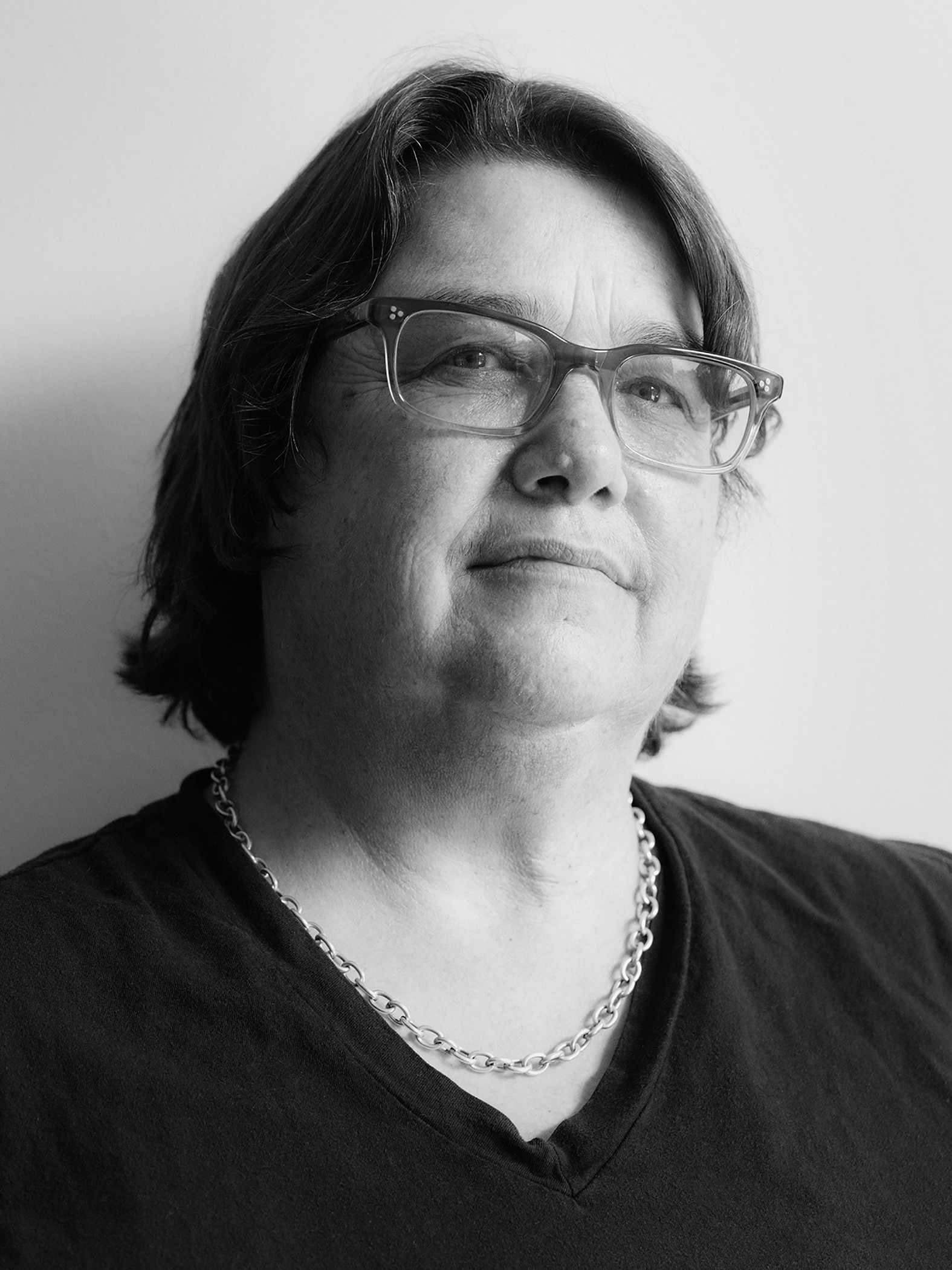 A black and white photograph of an older woman with glasses with head tilted up slightly, gazing at the camera