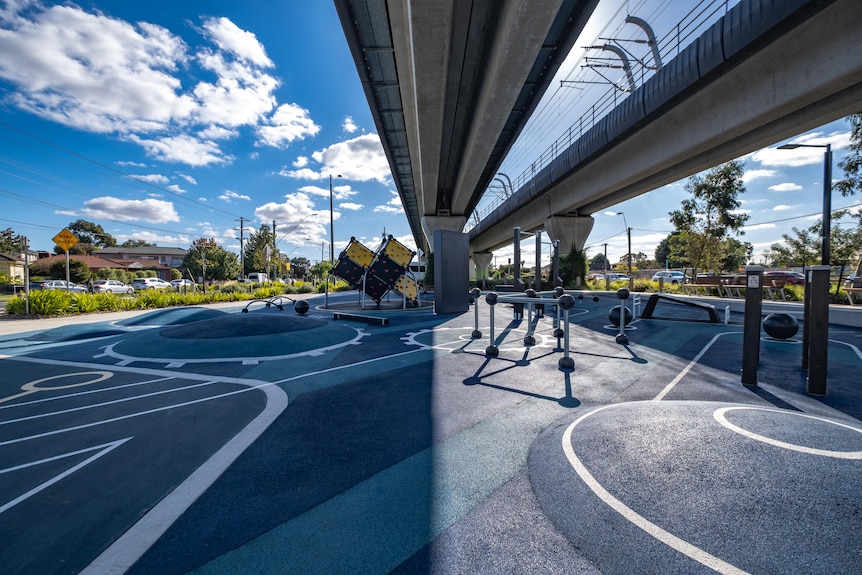 A view of light and shade and urban playground equipment under an above-ground railway in Clayton.