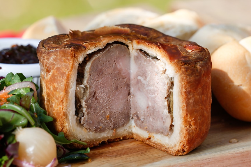 Photo of a dense pork pie with thick, golden pastry surrounding the entire pie. Inside is pink, firm meat.