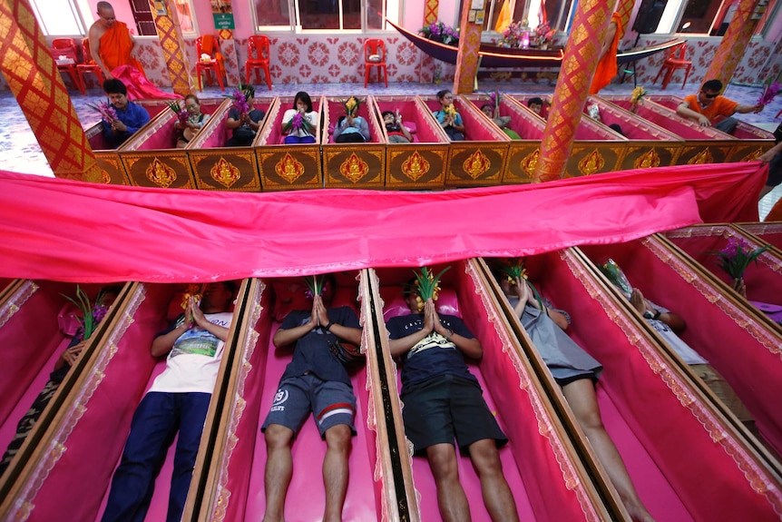 Over 20 people lie in pink coffins as a monk walks past them in a temple in Bangkok.