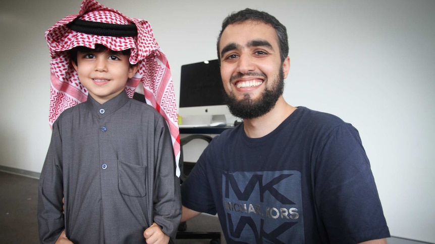 A father, wearing western clothes, and a boy, wearing traditional clothes from Saudi Arabia