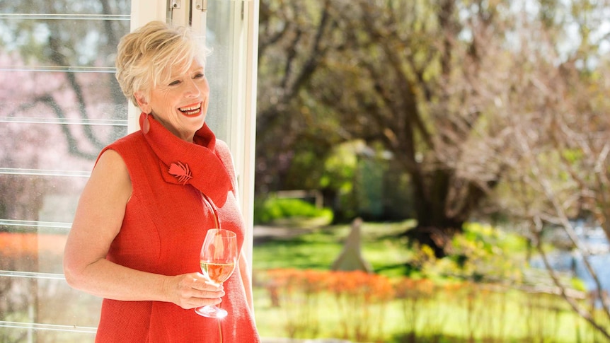 Woman in a red dress holding a glass of wine, looking out onto a garden