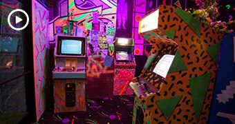 A very brightly coloured and patterned room, with three 80s-style video game machines.