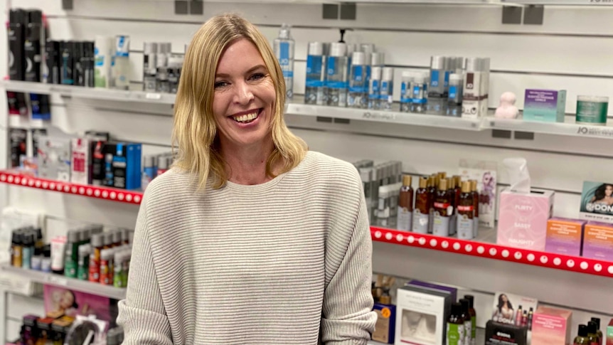 A woman smiles at the camera leaning on a shop counter