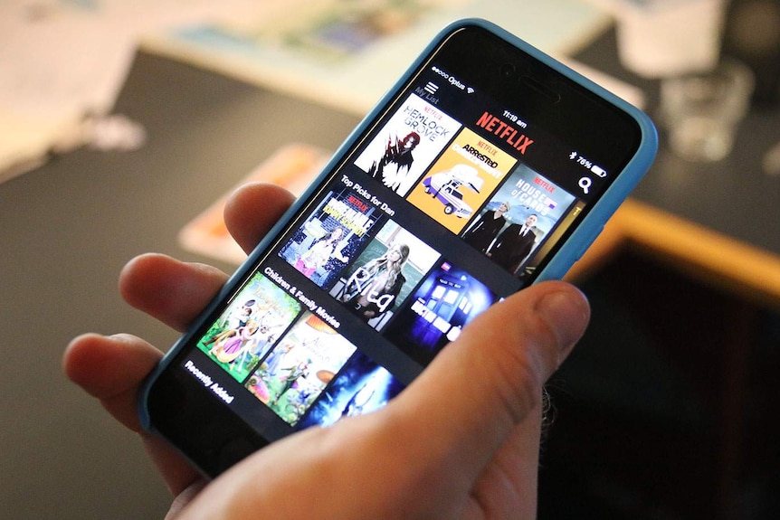 Hand holding a phone showing Netflix thumbnails 