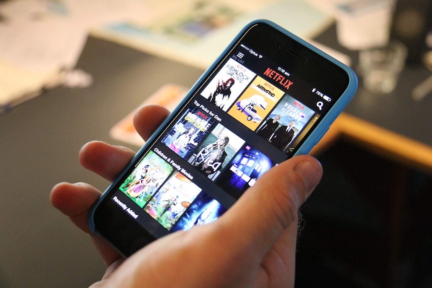 A person holds a mobile phone which displays Netflix