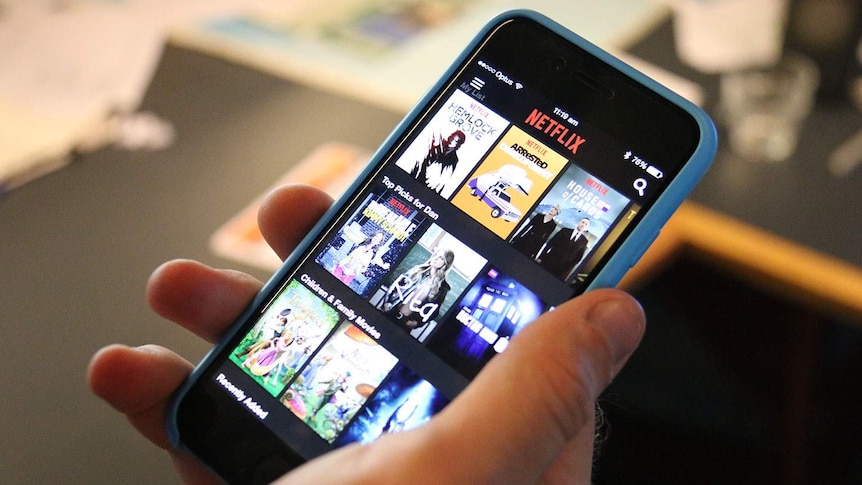 A hand holding a smart phone displaying the Netflix streaming app.