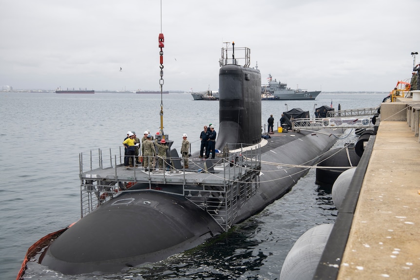 A group of people stand on top of a submarine at a dock