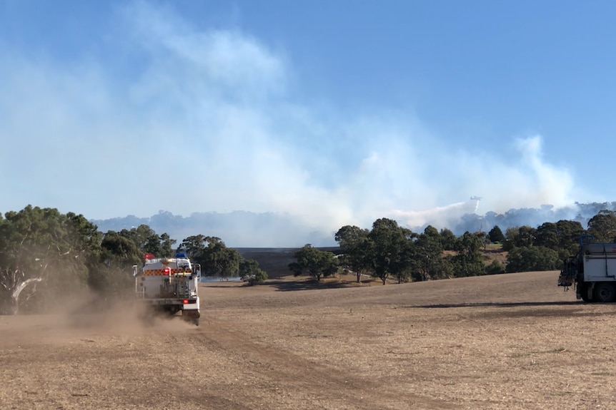An aerial firebomber flies over the Birdwood fire with a fire truck travelling in the foreground