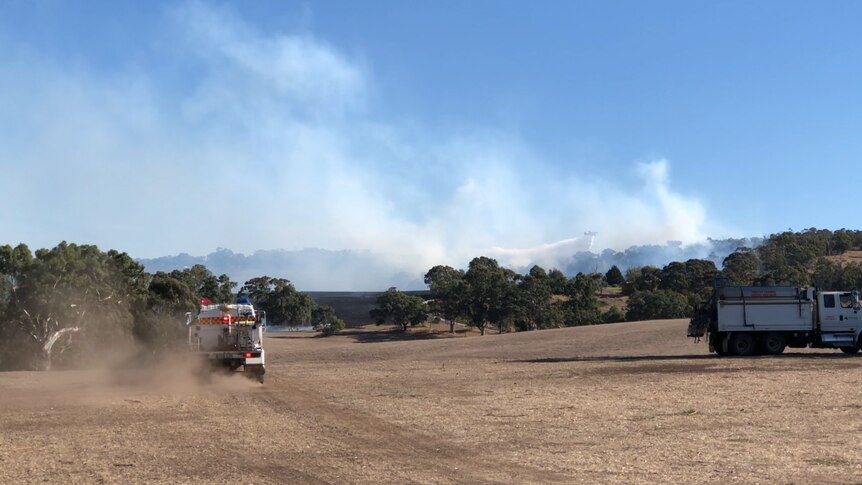 An aerial firebomber flies over the Birdwood fire with a fire truck travelling in the foreground