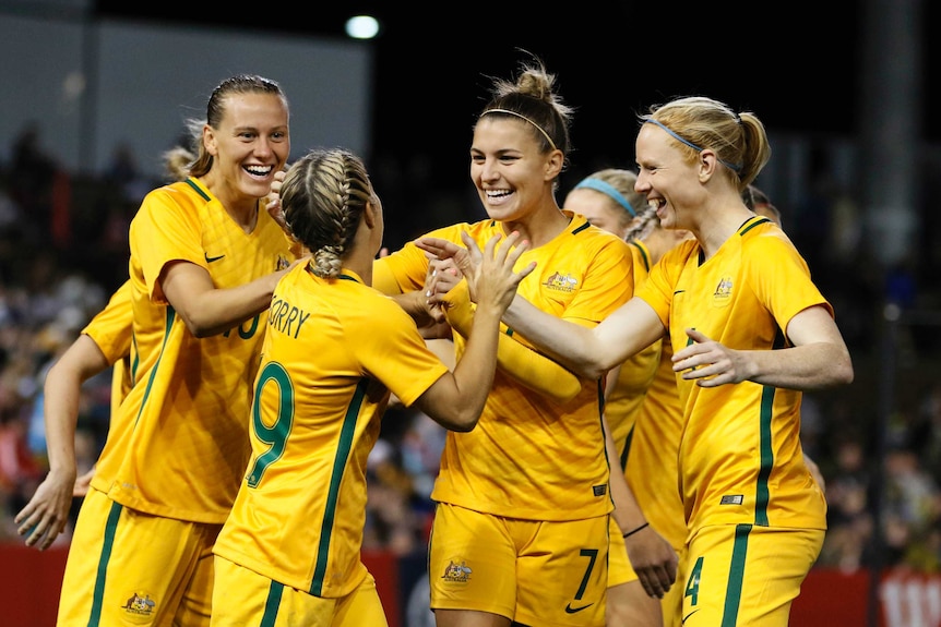 Matildas players smile and high-five after a Caitlin Foord goal.