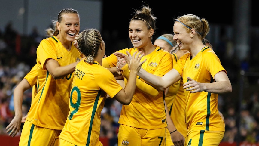Matildas players smile and high-five after a Caitlin Foord goal.