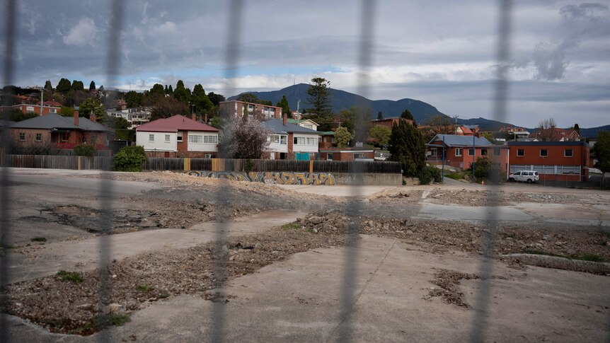 A cleared, flat construction site behind fencing amid houses.