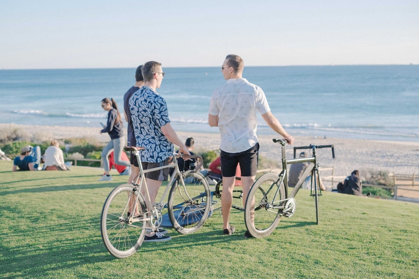 Three men look out to the ocean while holding their commuter bikes