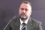 A man with a beard sits next to a microphone.