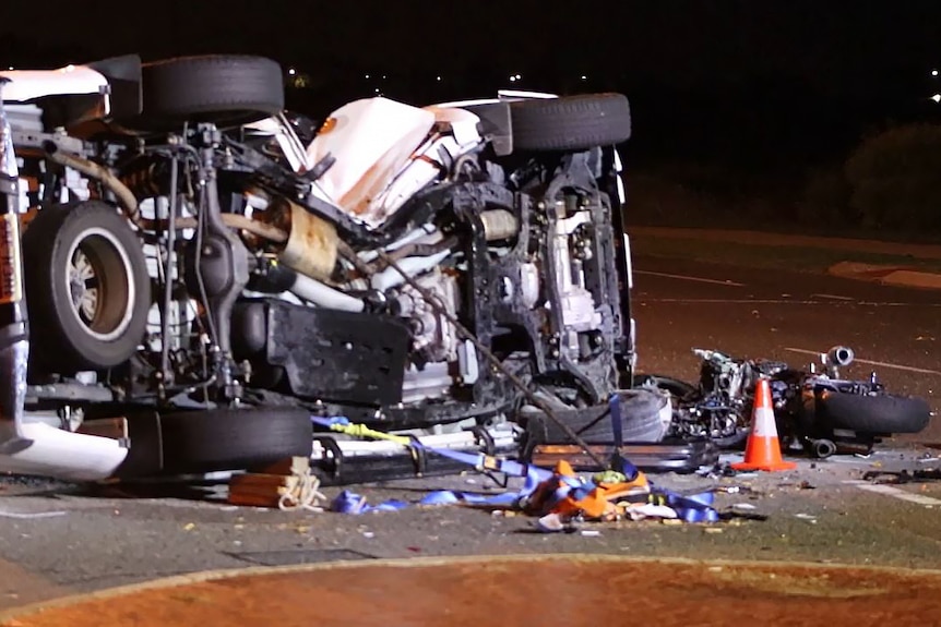 A white ute lies on its side after a crash with its undercarriage visible and a wrecked motorbike lying in front of the vehicle.