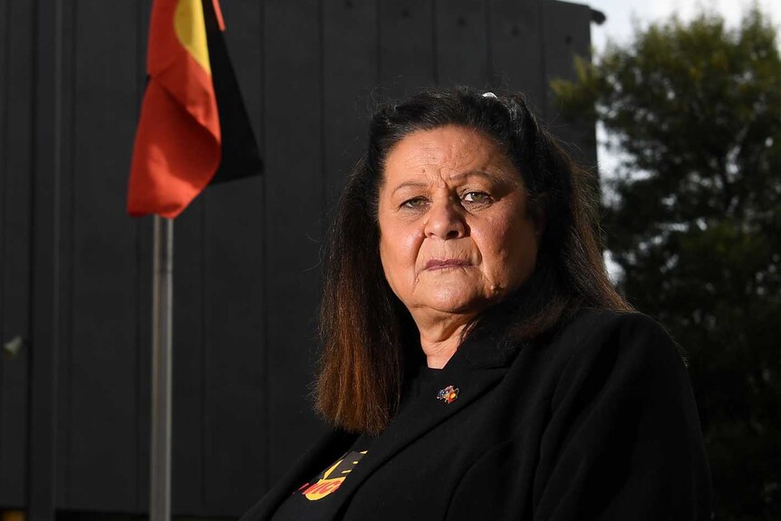 An Indigenous woman stares into the camera with the Indigenous flag on a flag pole behind her.