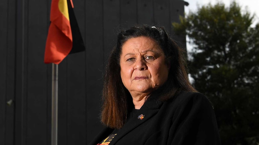 Jill Gallagher looks towards the camera as the Aboriginal flag flies on a flag pole behind her.