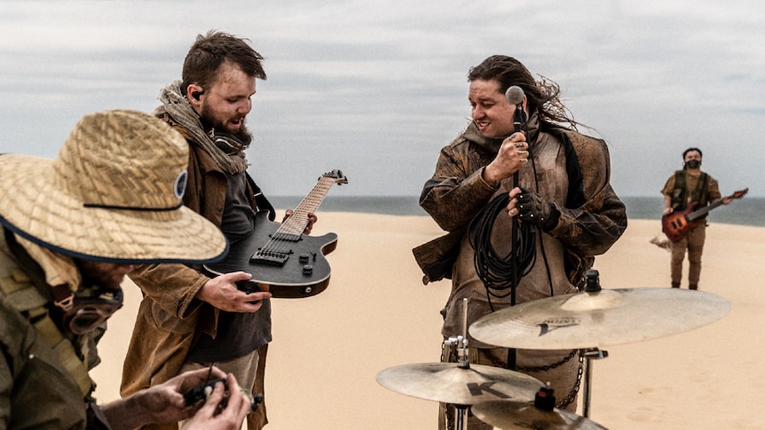 Polaris setting up drums, guitar and mic stand in the sand dunes