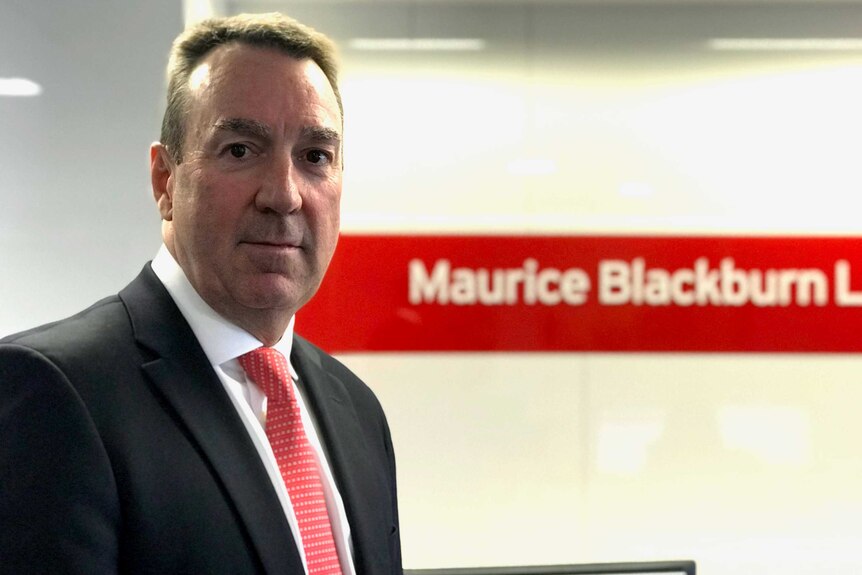 A man standing in front of a Maurice Blackburn sign.