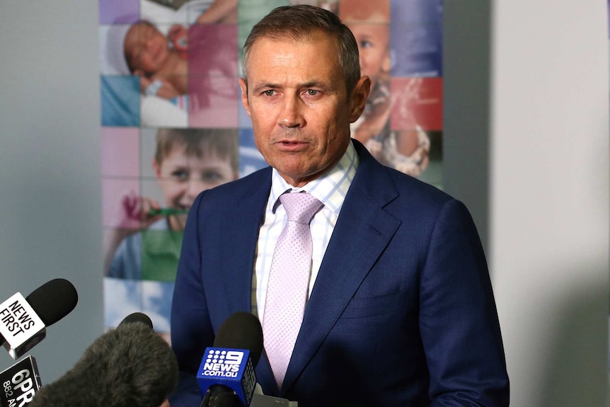 A mid-shot of WA Health Minister Roger Cook in a suit and tie talking indoors at a media conference.