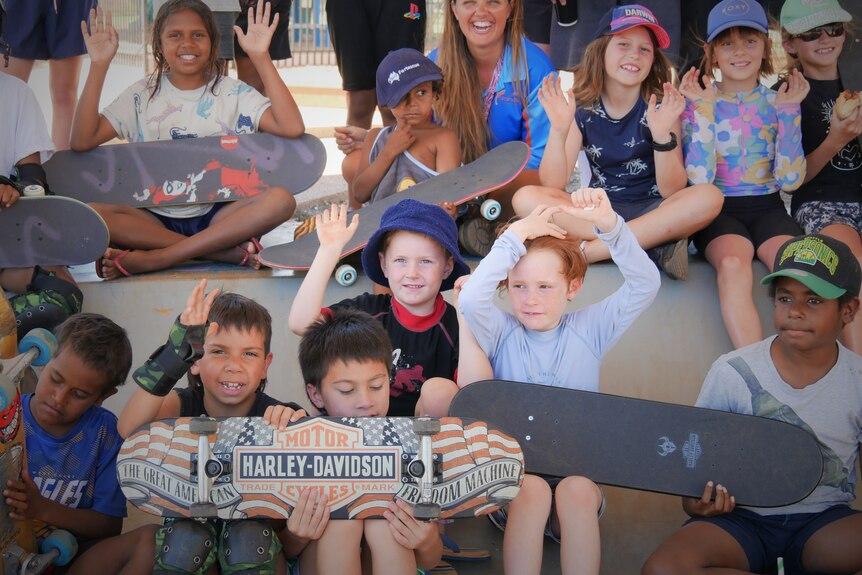 Kids smile and wave while holding skateboards
