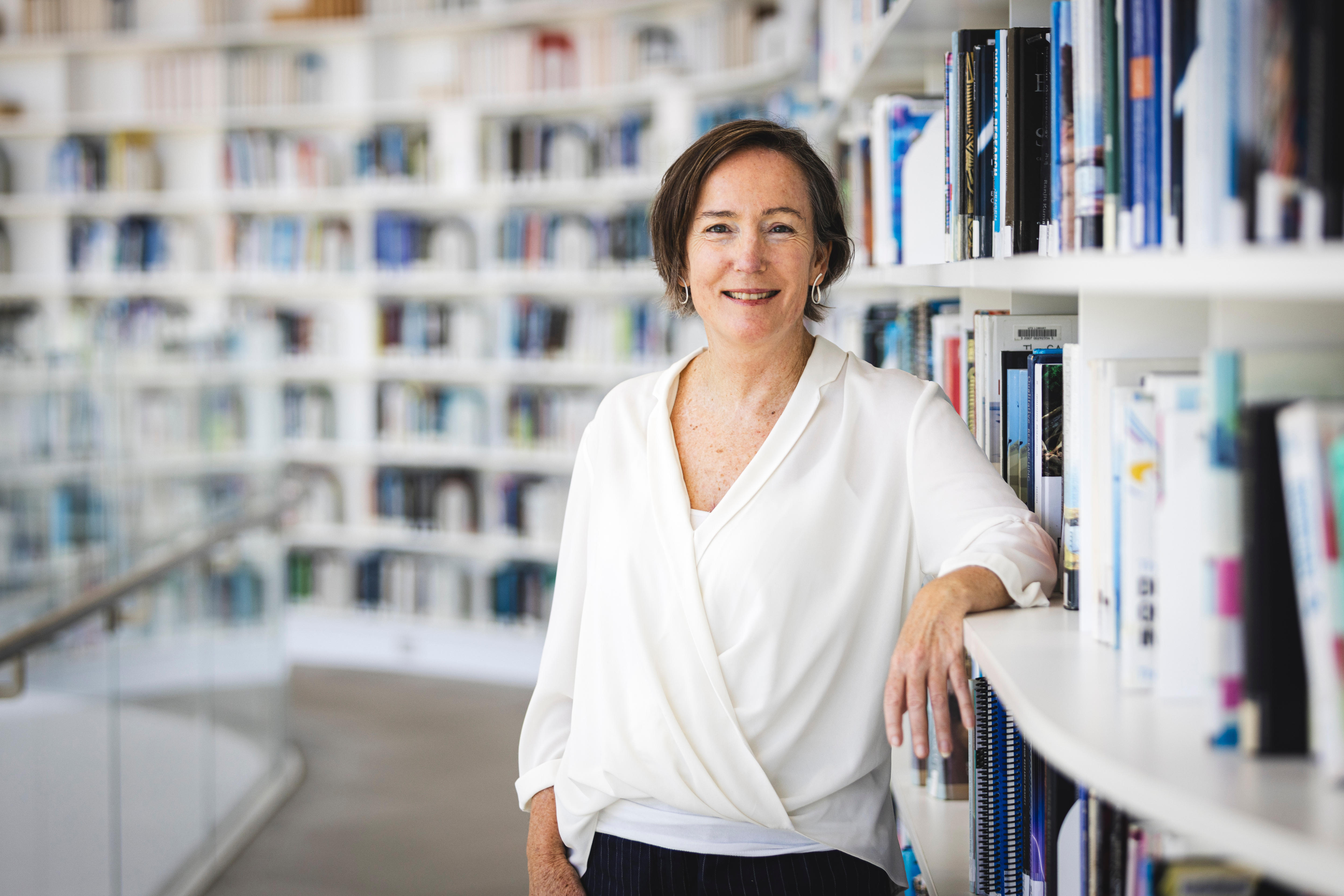 UTS Professor Jane Wangmann, wearing a white top, poses for a photo next to lots of book lined shelves