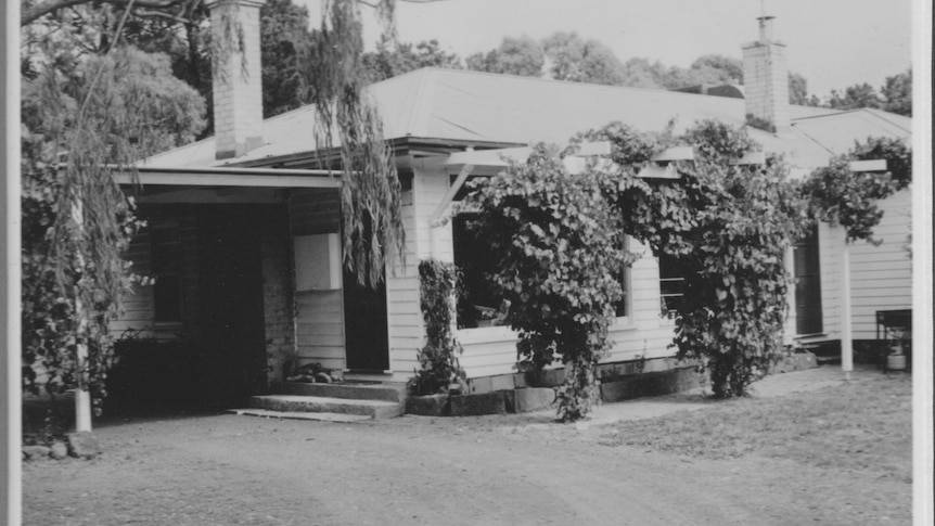 A black and white photograph of a weatherboard farmhouse