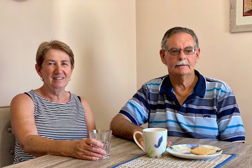 A man and woman sit at a table with a cup of tea and a glass of water. 