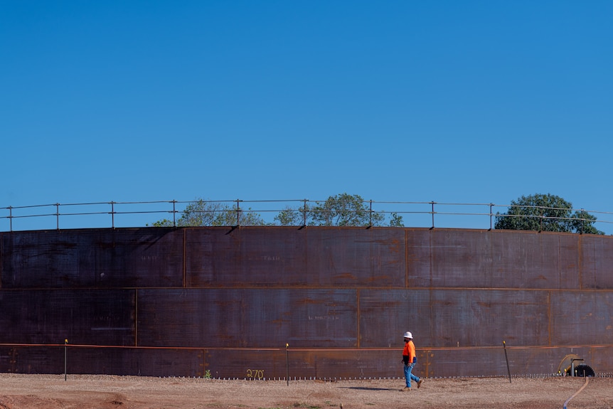 A man in high-vis walks past an enormous fuel storage tank